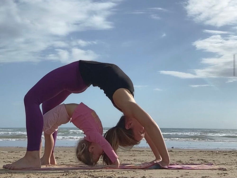 An adult and child doing gymnastics on the beach
