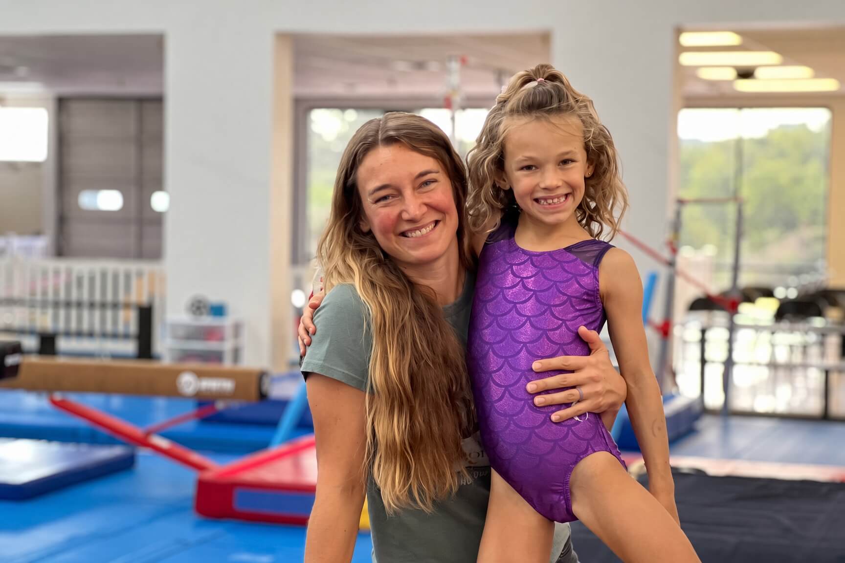 Coach hugging a smiling gymnast in a purple leotard