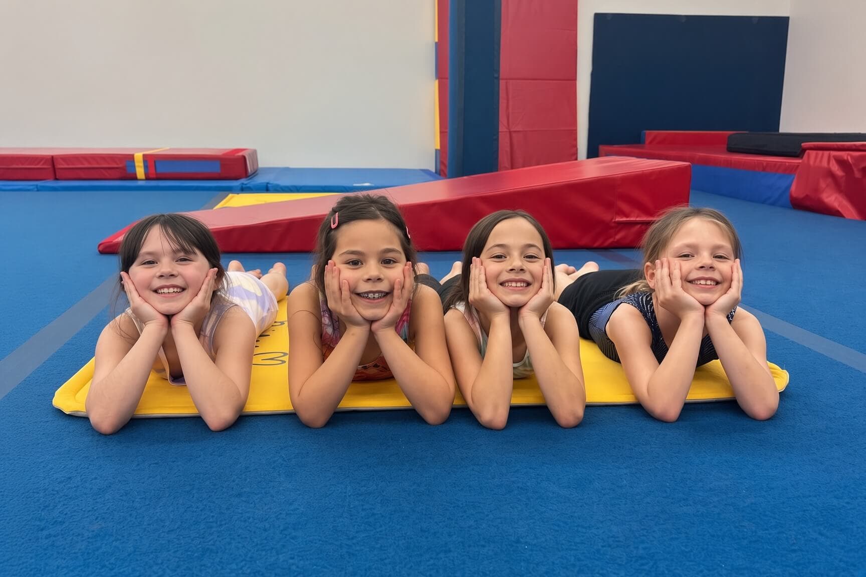Four gymnasts lying on a yellow mat, smiling at the camera