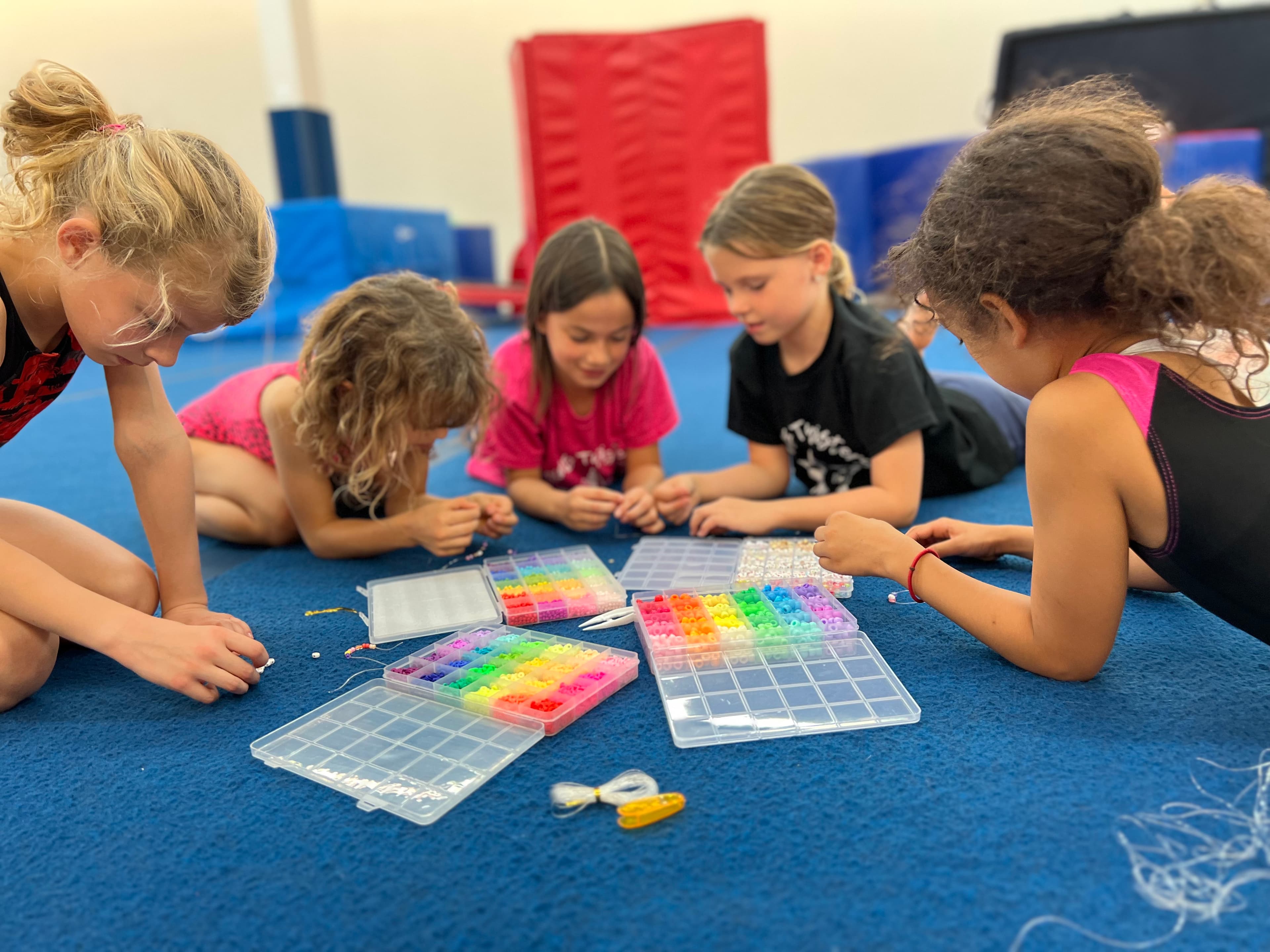 Kids making bead crafts on the gym floor at a birthday party