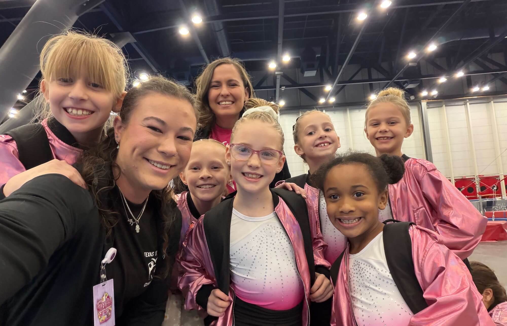 Coach talking with team gymnasts seated along the beam