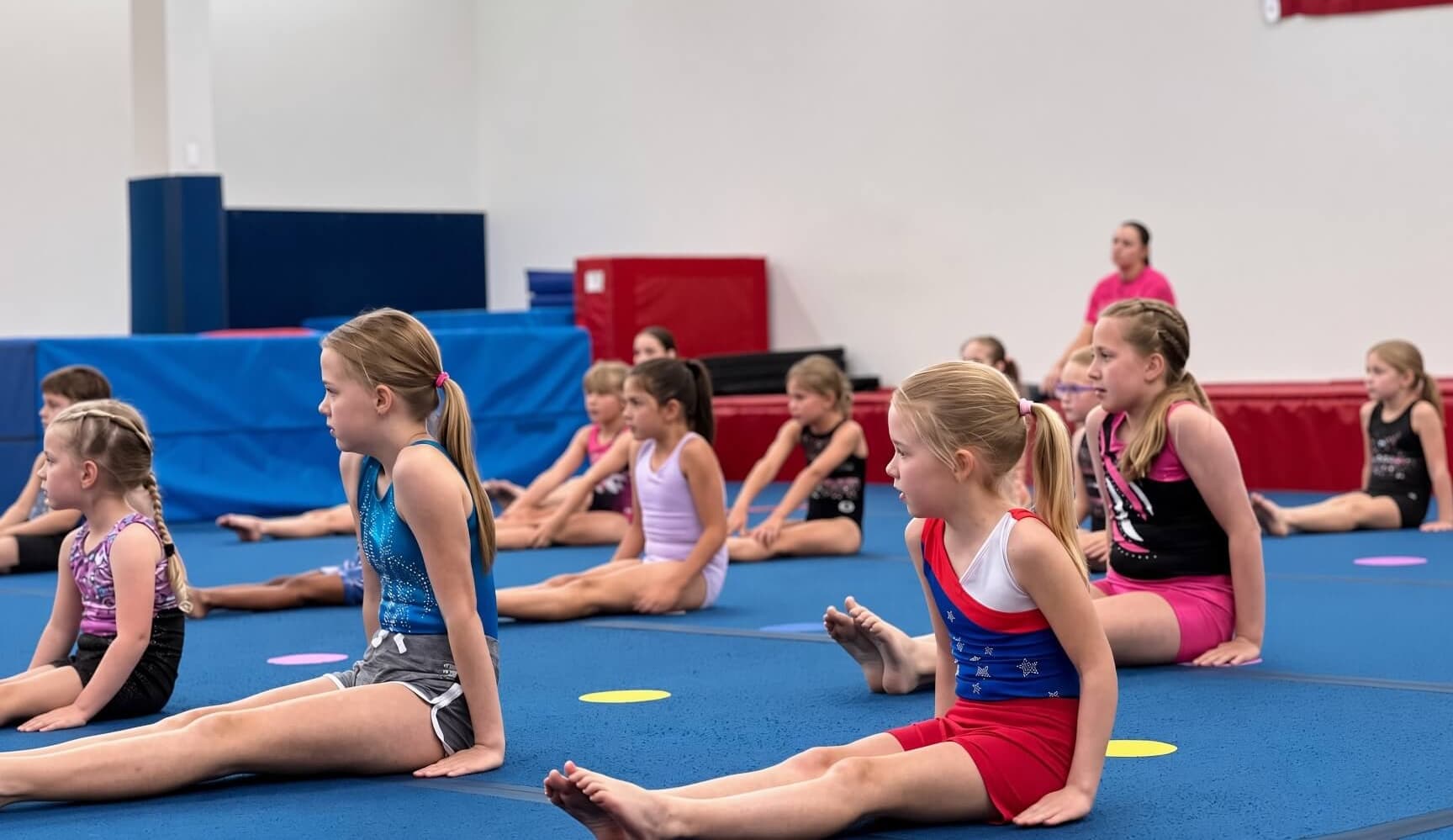 Tumbling class sitting in a straddle stretch on the floor